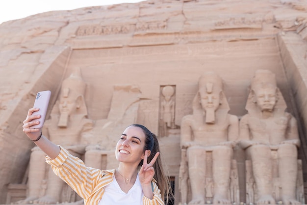 Gelukkige jonge vrouwelijke toerist die een selfie neemt met de beroemde tempel van Abu Simbel op de achtergrond