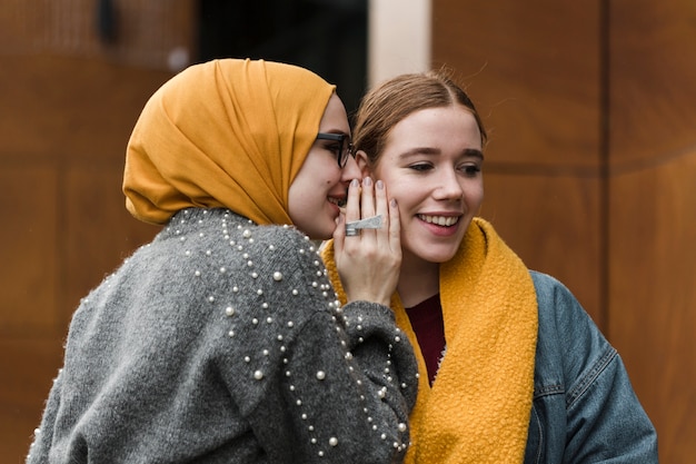 Gelukkige jonge vrouwen die aan elkaar fluisteren