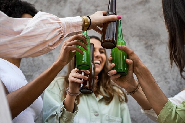 Gelukkige jonge vrouwen die samen plezier hebben met bierflesjes rammelen en samen buiten roosteren.