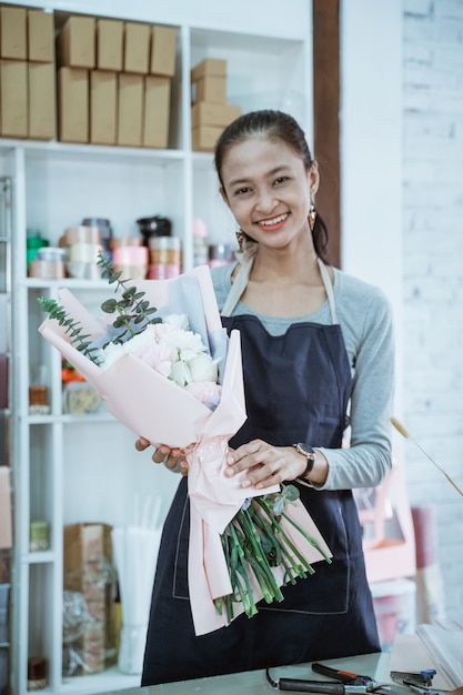 Gelukkige jonge vrouwenbloemist die in bloemenwinkel werken die flanellenbloem bekijken die de camera bekijken