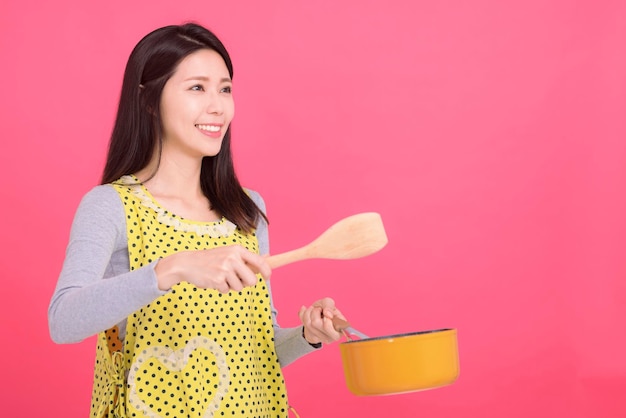 Gelukkige jonge vrouwenhuisvrouw die Keukenschort dragen terwijl het koken