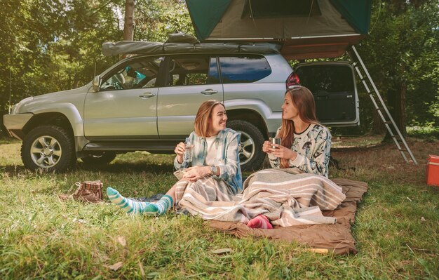 Gelukkige jonge vrouwenvrienden die onder een deken op de camping in het bos rusten