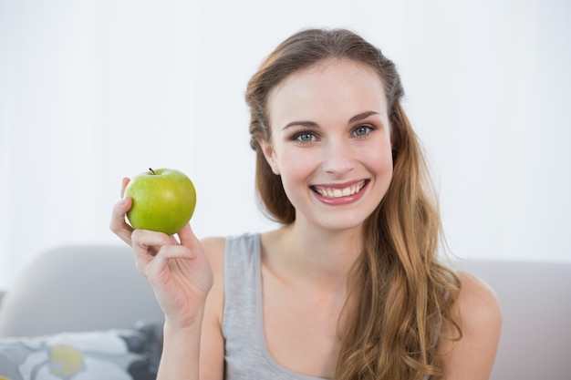 Gelukkige jonge vrouwenzitting op bank die groene appel houdt