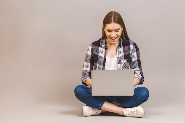 Gelukkige jonge vrouwenzitting op de vloer met gekruiste benen en het gebruiken van laptop