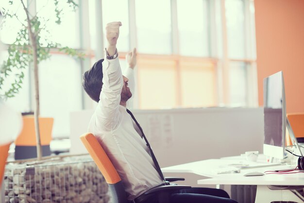 gelukkige jonge zakenman aan het werk op een desktopcomputer aan zijn bureau in een modern, helder startup-kantoorinterieur