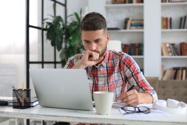 Gelukkige jonge zakenman analyseert financiële documenten vanuit huis tijdens zelfisolatie.