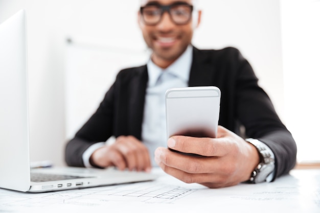 Foto gelukkige jonge zakenman die mobiele telefoon gebruikt terwijl hij op kantoor werkt