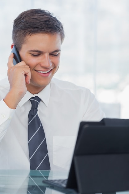 Gelukkige jonge zakenman op de telefoon terwijl het werken aan zijn tablet