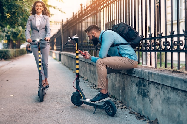 Gelukkige jonge zakenpartners die samen genieten tijdens het rijden op elektrische scooters op straat in de stad.