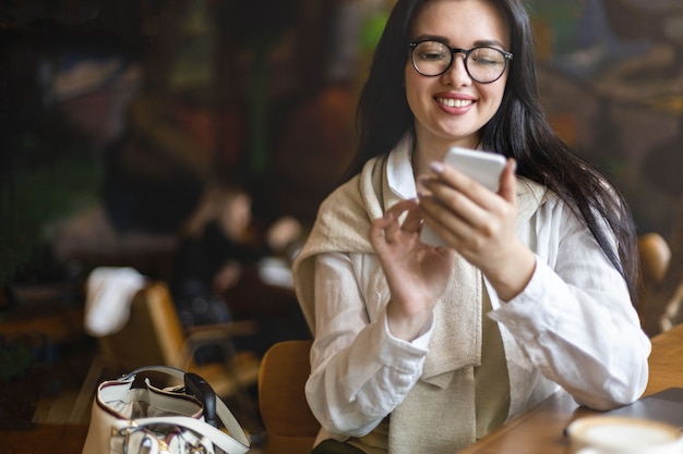 Gelukkige jonge zakenvrouw die aan het chatten is, gebruikt een smartphone die in de hal van het moderne winkelcentrum zit