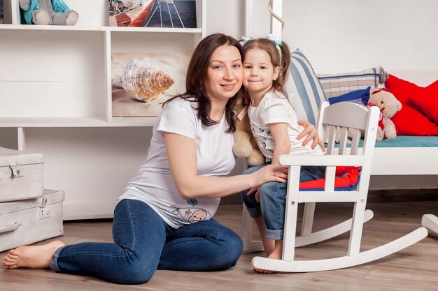 Gelukkige jonge zwangere moeder met driejarig meisje in de kinderkamer en camera kijken. Leuke familie, moeder en dochter in huis en spelen. Sfeervolle familiemomenten voor baby's. Ruimte kopiëren