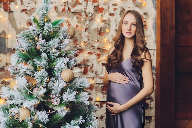 Gelukkige jonge zwangere vrouwenzitting dichtbij de Kerstboom