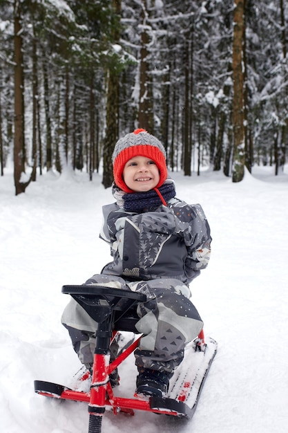 Gelukkige jongen bergafwaarts op een slee in de winter zit een kind in lichte kleren op een slee sneeuw vliegt naar hem