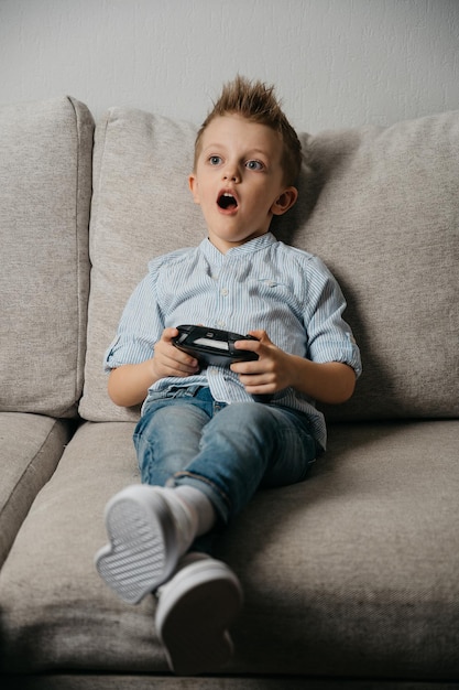 Gelukkige jongen die videogames speelt met een gamecontroller die op de coach in de woonkamer zit