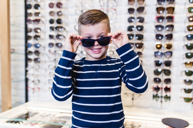Gelukkige jongen die zonnebril kiest in optische winkel.