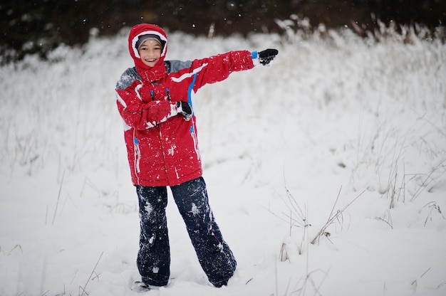 Gelukkige jongen draagt rode jas op winterdag. Wandelen in het park op koude dag met sneeuw.