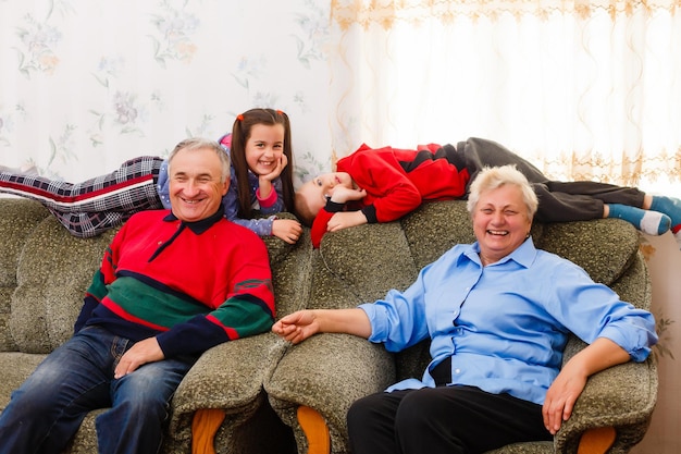 Gelukkige jongen en meisje met hun lachende grootouders die naar de camera glimlachen terwijl ze samen binnenshuis poseren