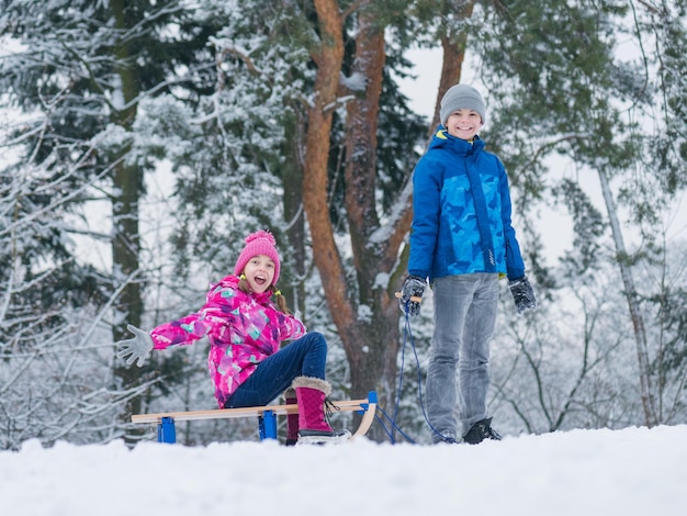 Gelukkige jongen en meisje rijden op de slee en hebben plezier Kinderen spelen buiten in de sneeuw slee Kinderen slee in het besneeuwde park in de winter Buitenplezier voor familie Kerstvakantie