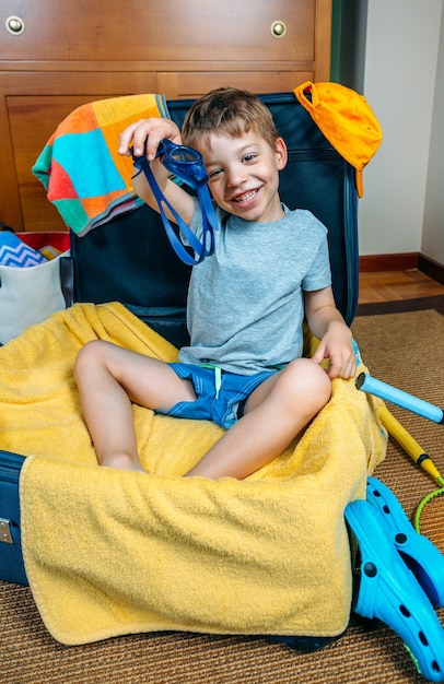 Gelukkige jongen glimlachend zittend in een koffer klaar om op vakantie te gaan met een zwembril