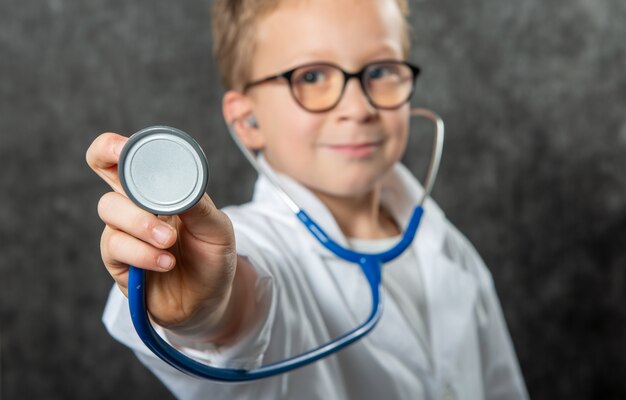 Gelukkige jongen in de holdingssthetoscope van het artsenkostuum