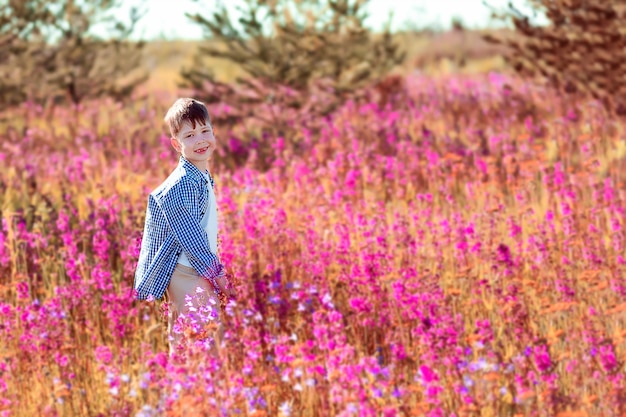 Gelukkige jongen in een veld met heldere bloemen. een veld met roze bloemen. jongen plukt bloemen in het veld