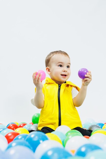 Gelukkige jongen in kleurrijke ballen in de speelgroep van kinderen het kind glimlacht verborgen in de ballen