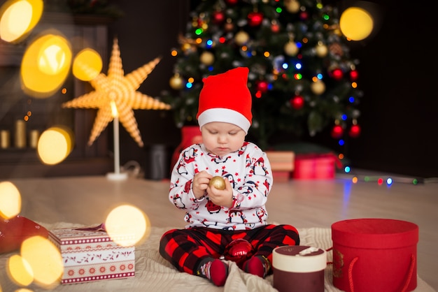 Gelukkige jongen, kind in een rode kerstmuts zit met kerstversiering