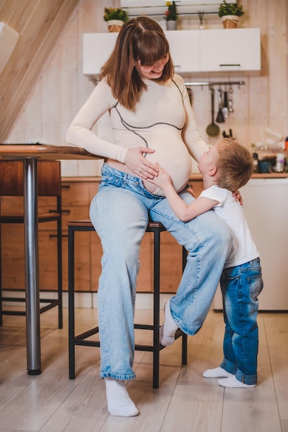 Gelukkige jongen knuffelen en aanraken van de buik van zwangere moeder