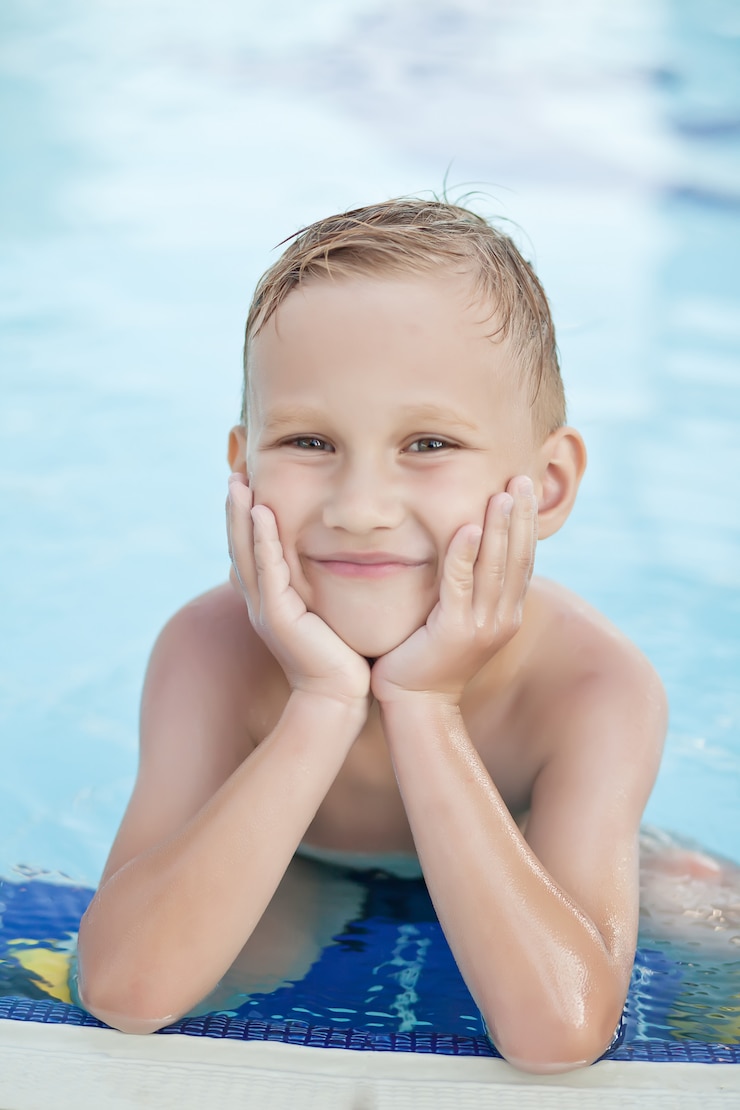 Foto gelukkige jongen met blonde haar het glimlachen zitting in zwembad