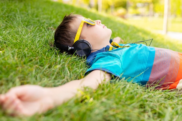 Gelukkige jongen met zonnebril die op het gras ligt en naar muziek luistert in koptelefoon