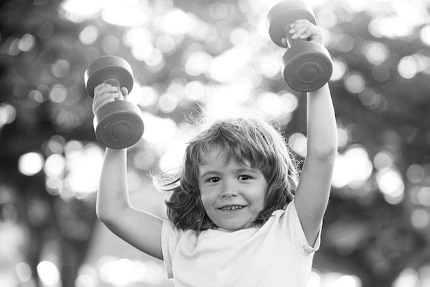 Gelukkige jongen training met halter in park Sportieve activiteit Kid sport Kind oefenen buiten