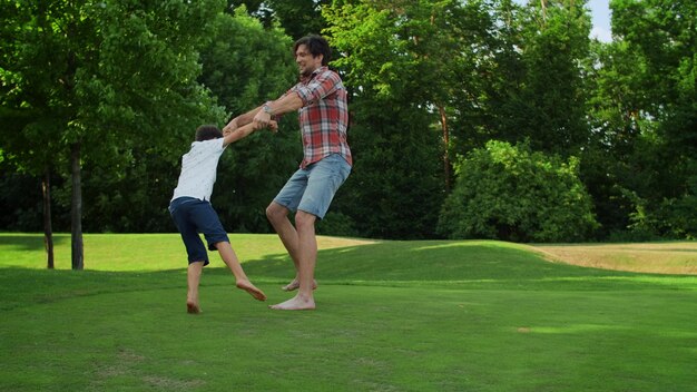 Foto gelukkige jongen uitgevoerd in zomer park lachende man spinnende jongen in groene weide