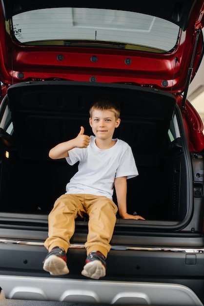 Gelukkige jongen zit in de kofferbak van een nieuwe auto bij een dealer. Een auto kopen.