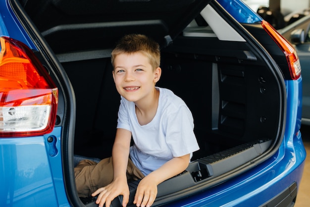 Gelukkige jongen zit in de kofferbak van een nieuwe auto bij een dealer