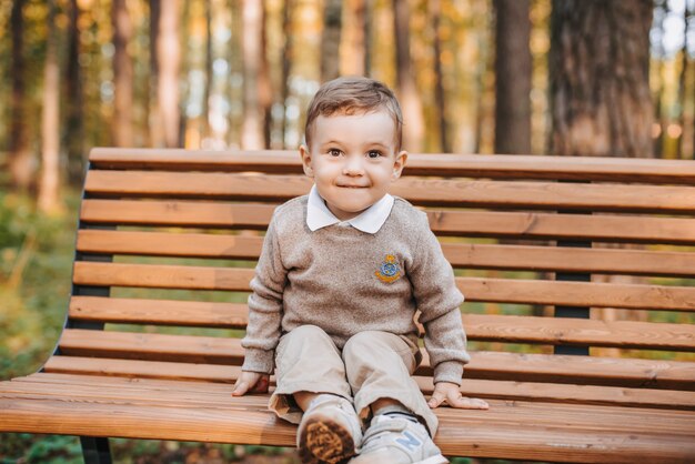 Gelukkige jongen zittend op een bankje in het park in de herfst