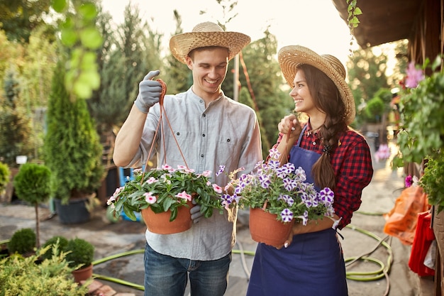 Gelukkige jongens- en meisjestuiniers in strohoeden houden potten met petunia op het tuinpad op een zonnige dag. .