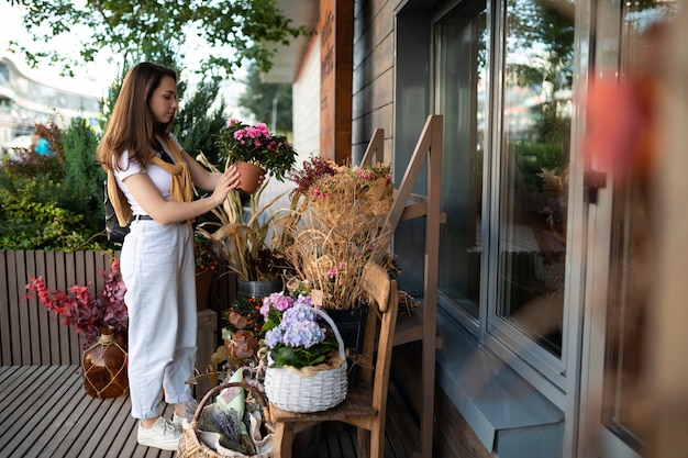 Gelukkige kaukasische jonge vrouw kiest potbloemen om te kopen bij de tuinkraam buiten