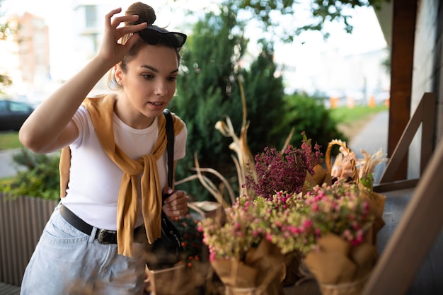 Gelukkige kaukasische jonge vrouw kiest potbloemen om te kopen bij de tuinkraam buiten