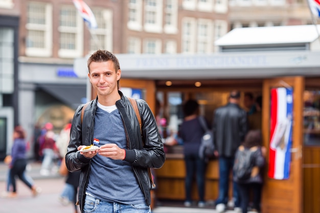 Gelukkige kaukasische toerist met verse haringen met ui en netherlandvlag in amsterdam.