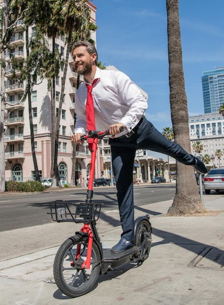 Gelukkige kerel in formalwear rijden stand-up e-scooter langs stoep, actief.