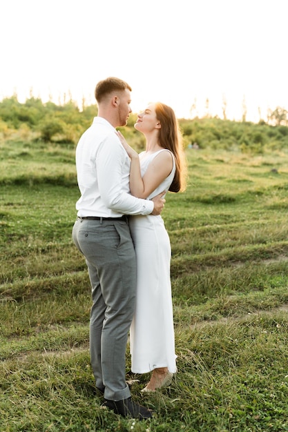 Gelukkige kerel knuffelt zijn bruid bij zonsondergang van de dag. portret van een verliefd stel. gelukkige jonge mensen met een europees uiterlijk. zomer huwelijksreis dag