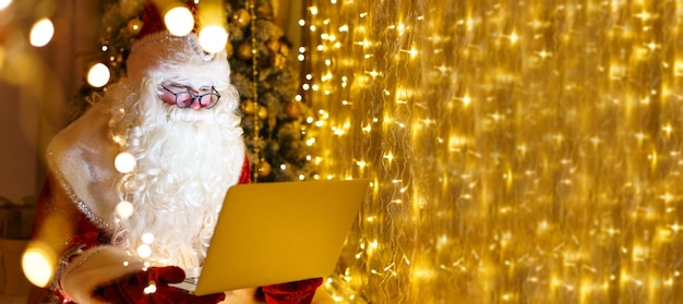 Gelukkige kerstman in pak zittend op een fauteuil met laptop op kerstavond online e-commerce winkel...