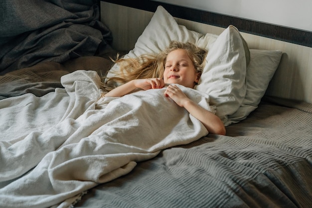 Gelukkige kind ligt op het bed onder een witte deken op het kussen slapen