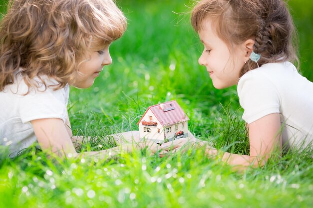 Gelukkige kinderen die modelhuis in handen houden Kinderen liggen op groen gras in het voorjaarspark Nieuw huisconcept