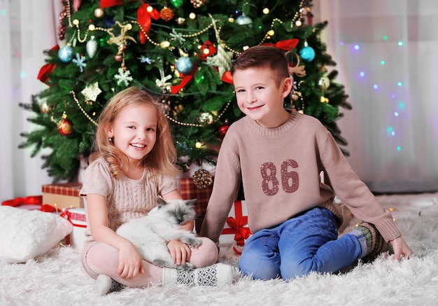 Gelukkige kinderen en pluizige kat in de versierde kerstkamer