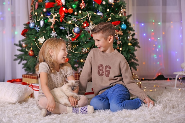 Gelukkige kinderen en pluizige kat in de versierde kerstkamer