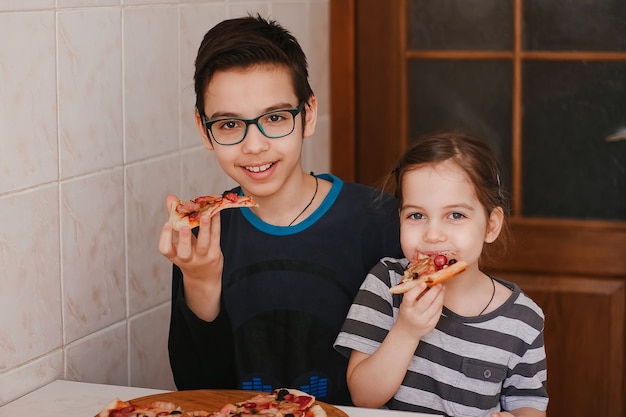Gelukkige kinderen, jongen en meisje die pizza thuis eten