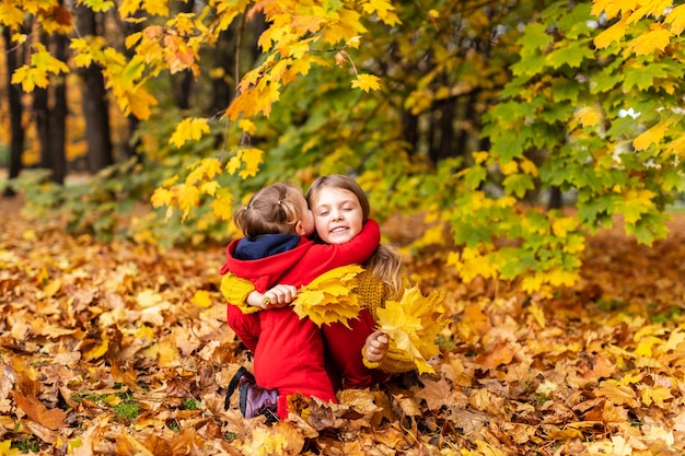 Gelukkige kinderen, kleine meisjes knuffelen in gele esdoornbladeren in het herfstpark buiten