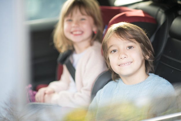 gelukkige kinderen meisje met haar broer zitten samen in moderne auto kinderzitjes vergrendeld met veiligheidsgordels