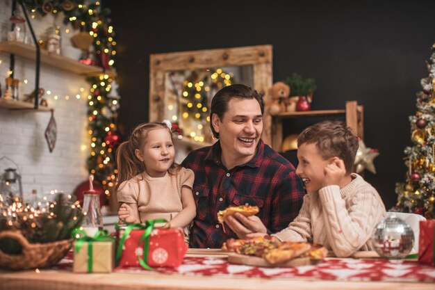 Gelukkige kinderen met papa pizza eten in de keuken ingericht voor Kerstmis